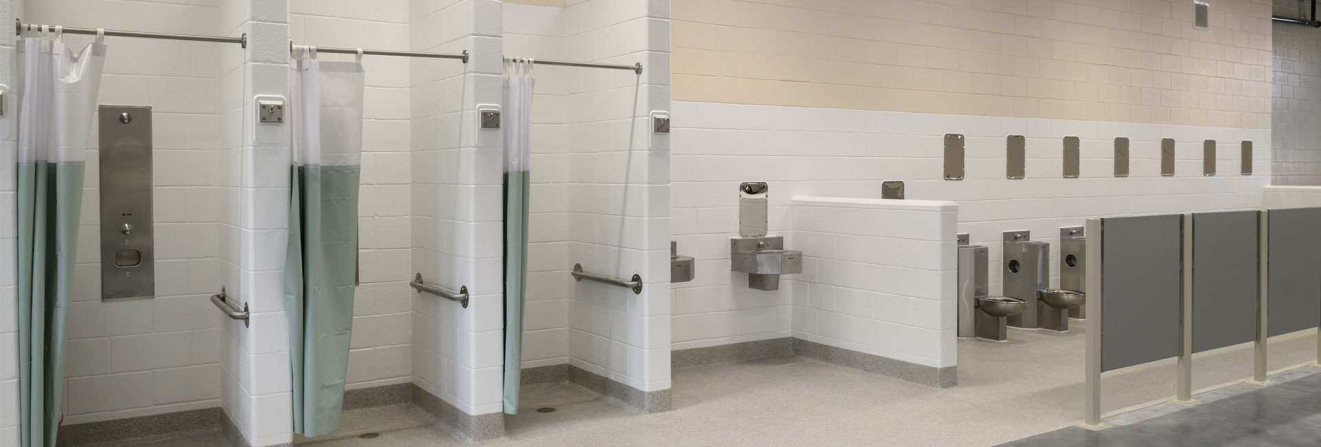 The Volusia County Branch Jail bathroom with white tile walls and stainless steal fixtures, sinks, toilets, handrails and partitions, built by the Ajax Building Company.