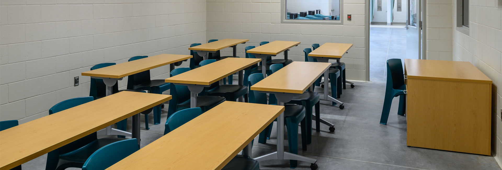 A room with wooden and metal desks and green chair facing forward at the Volusia County Branch Jail built by Ajax Building Company.