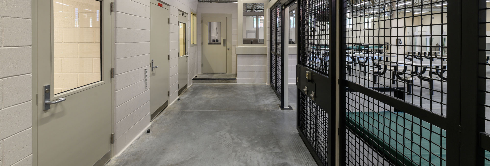 Black metal gates leading to the dorm of the Volusia County Branch Jail with white walls on opposite side and various doors built by the Ajax Building Company.